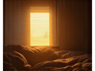 Sunlight streaming through blinds onto a bed in the early morning, showing someone awake too early.